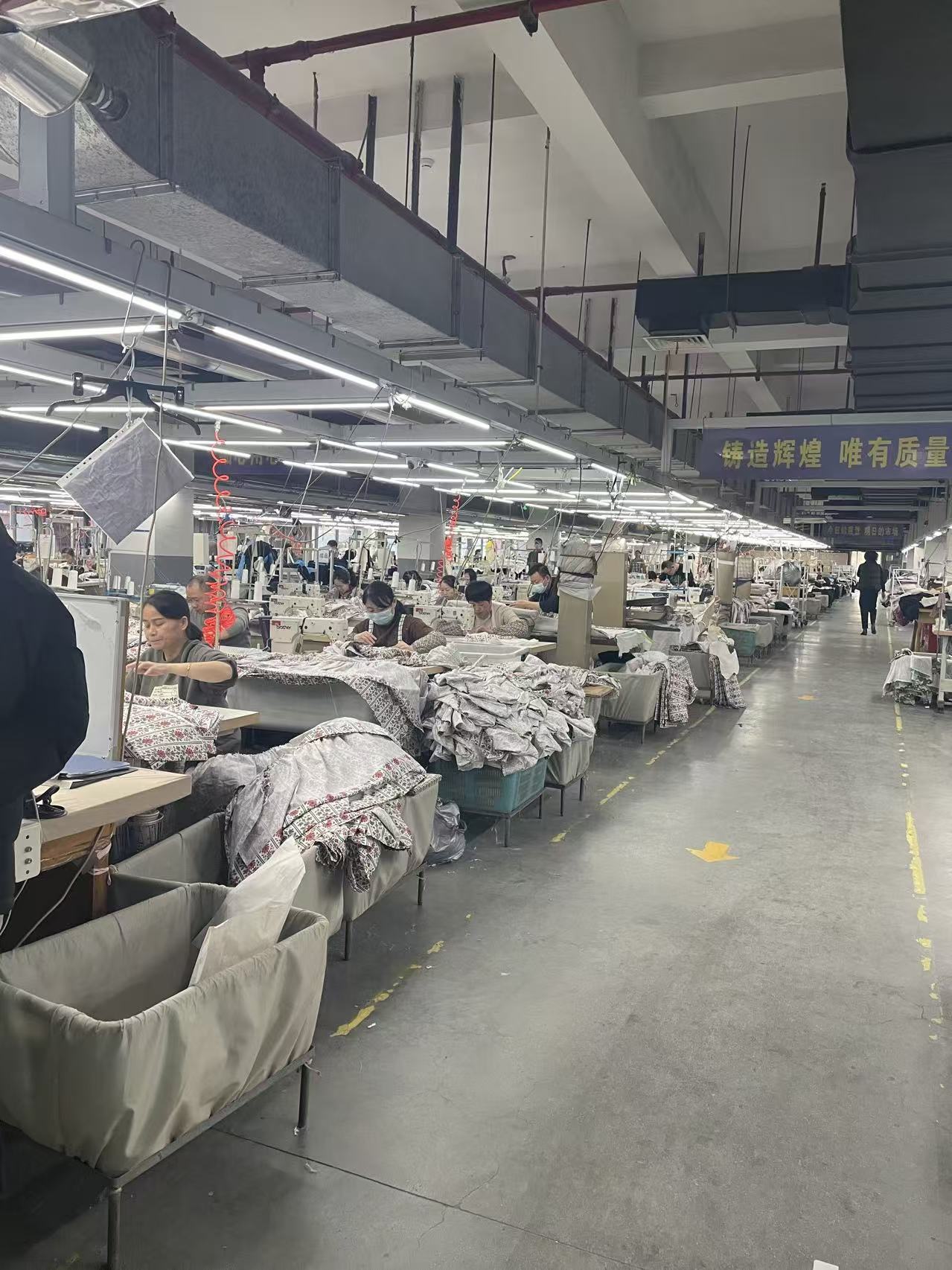 One of Deepwove's four full-time pattern makers at her cutting table in the Hangzhou workshop — paper pattern half-cut, French curve in hand, a half-pinned muslin toile on the dress form beside her, mid-conversation with a designer pointing at the bodice darting.