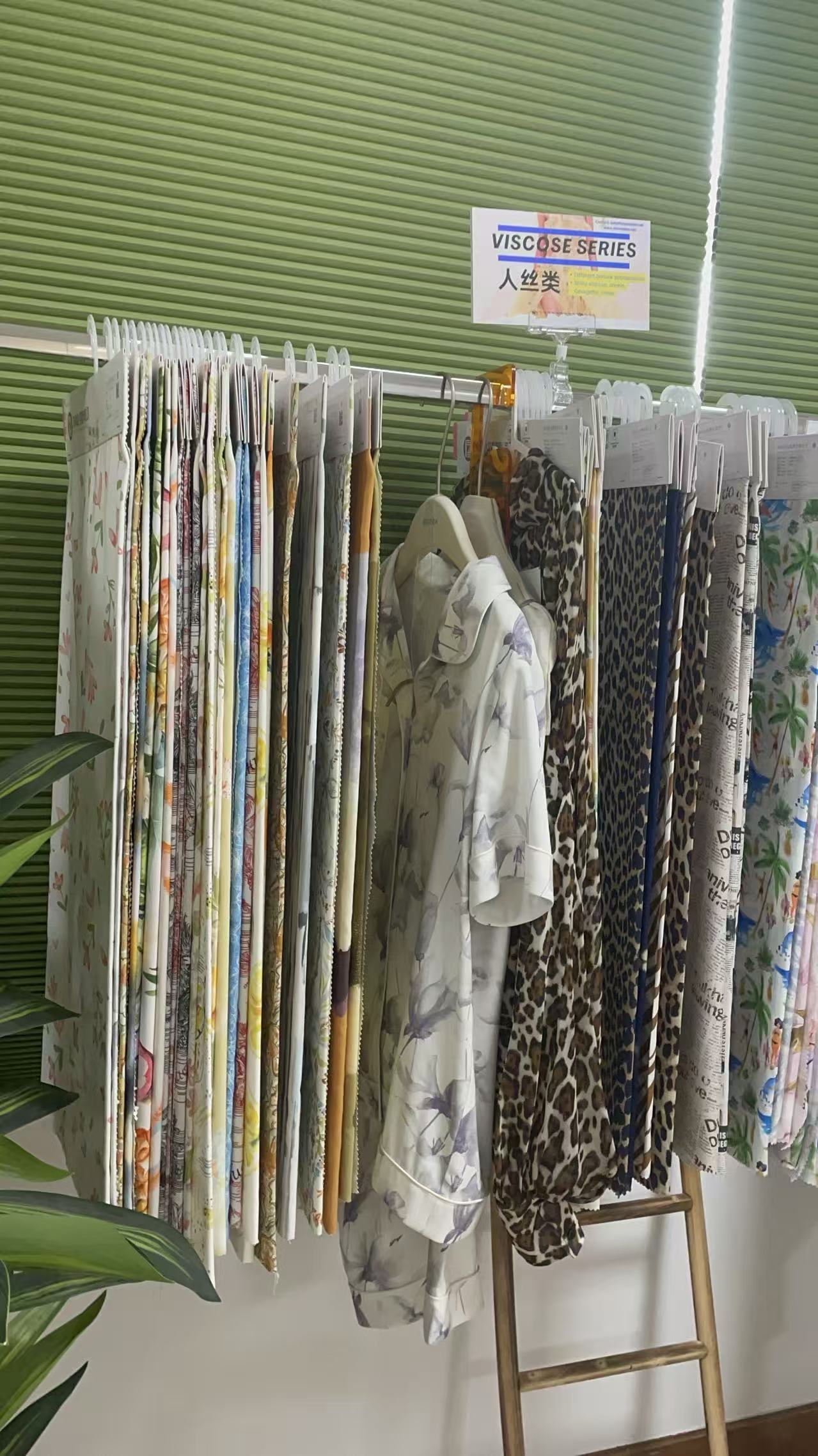 A Deepwove fabric rack inside the Hangzhou workshop showing a variety of silk and silk-blend fabric swatches organized for sourcing reference, with Chinese labels marking the fabric series