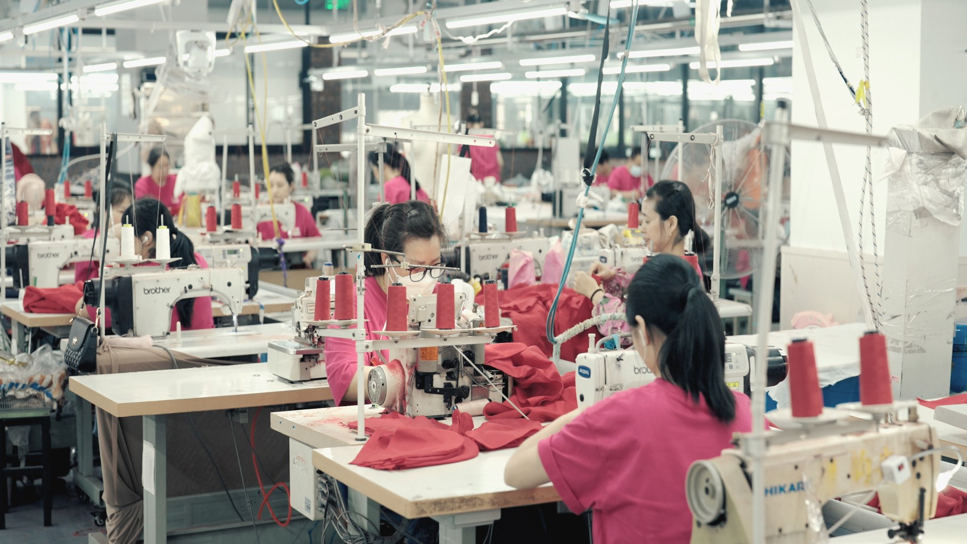 Production floor with multiple sewing lines and organized fabric stock alongside