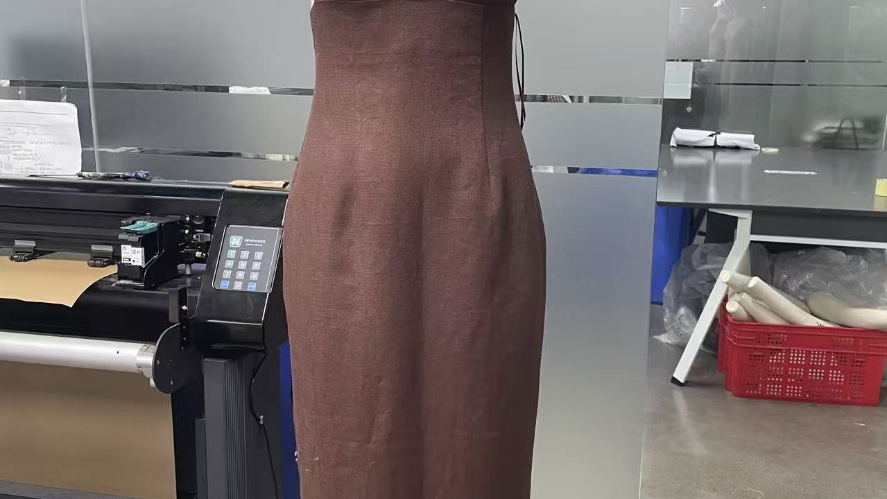 Pattern making cutting room at Deepwove's Hangzhou studio — linen dress on dress form beside an industrial cutting table and paper pattern rolls used during sample development
